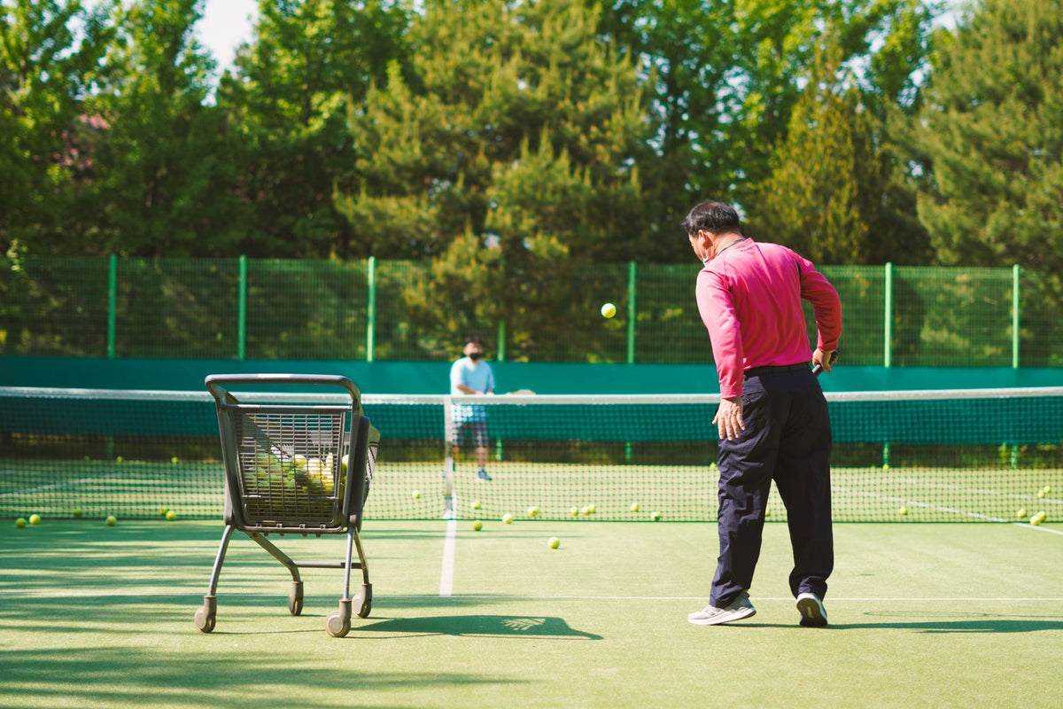 Two tennis players practising beside a ball cart
