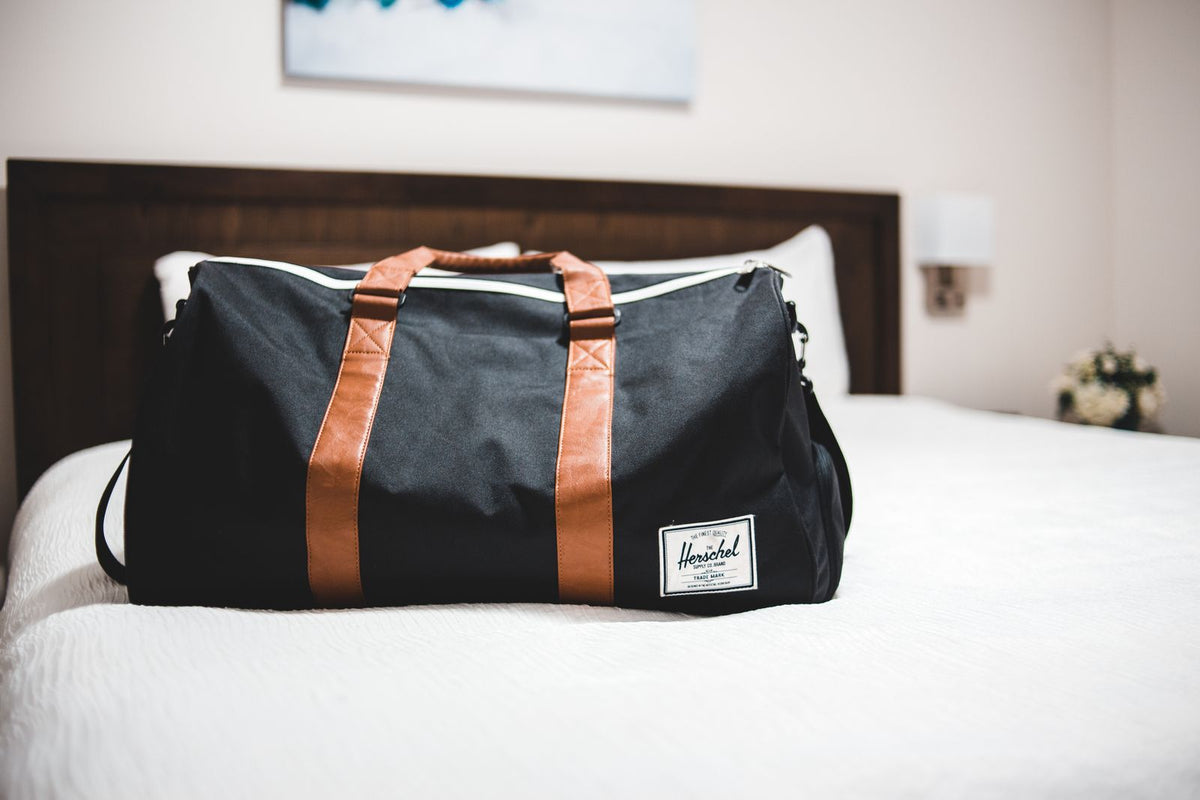 Black duffel bag with brown handles resting on a hotel bed