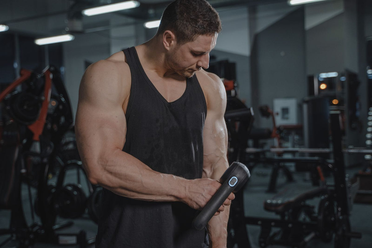Man using a handheld massage gun in a gym