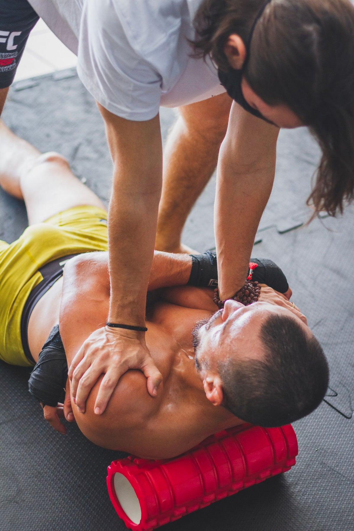 Trainer helping an athlete use a foam roller indoors