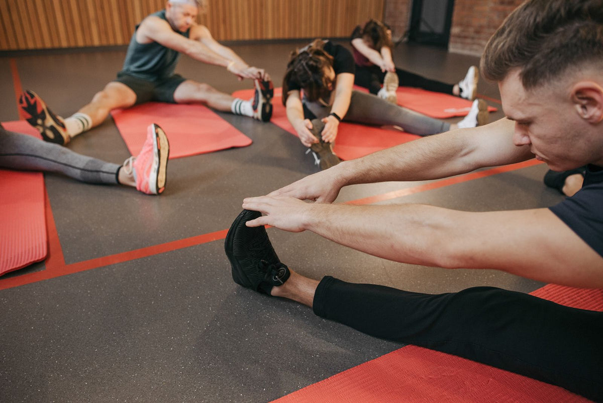 Adults stretching their legs on exercise mats indoors