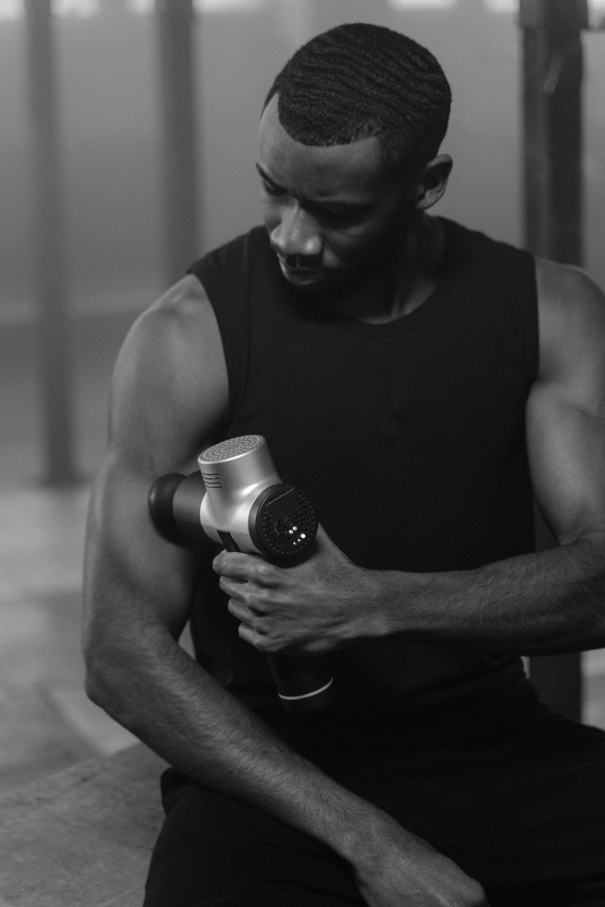 Athlete using a handheld massage gun in a gym