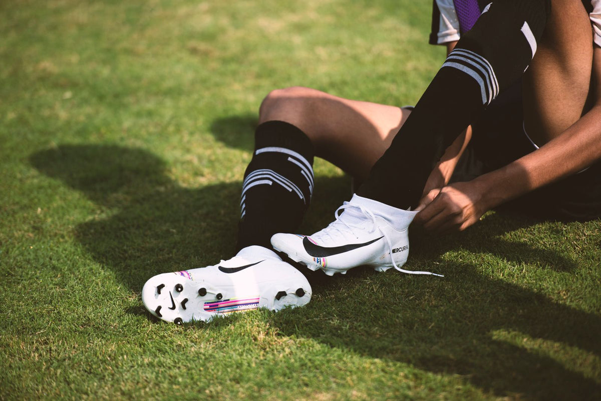 Soccer player lacing football boots beside a playing field